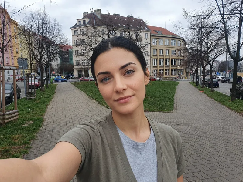 Accompanying digital illustration: a close view of Tereza in Danner Park, with paved paths, a lawn, trees and surrounding buildings behind her.