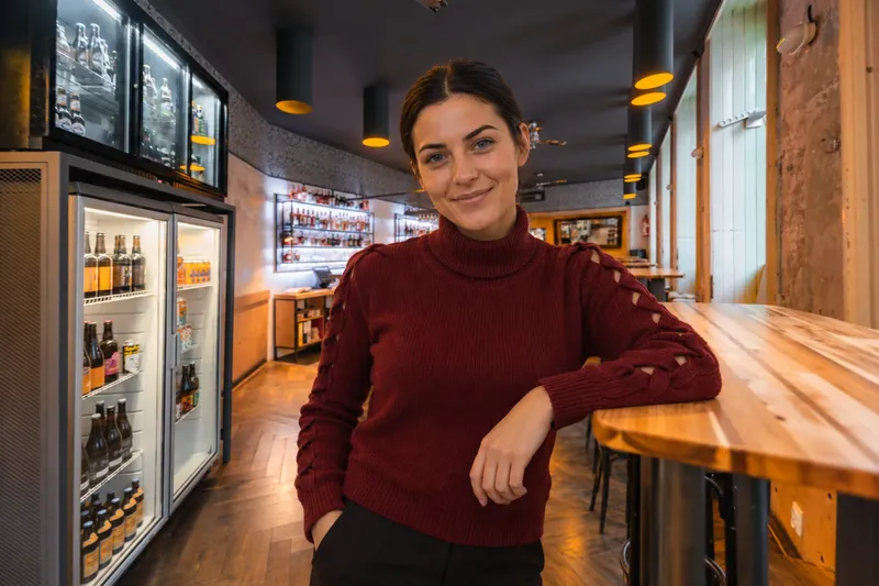 Tereza in a burgundy rollneck sweater leaning against the wooden counter inside Bad Flash Bar.